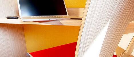 Un espacio de trabajo moderno con una laptop sobre un escritorio de madera, una silla roja y una pared amarilla.