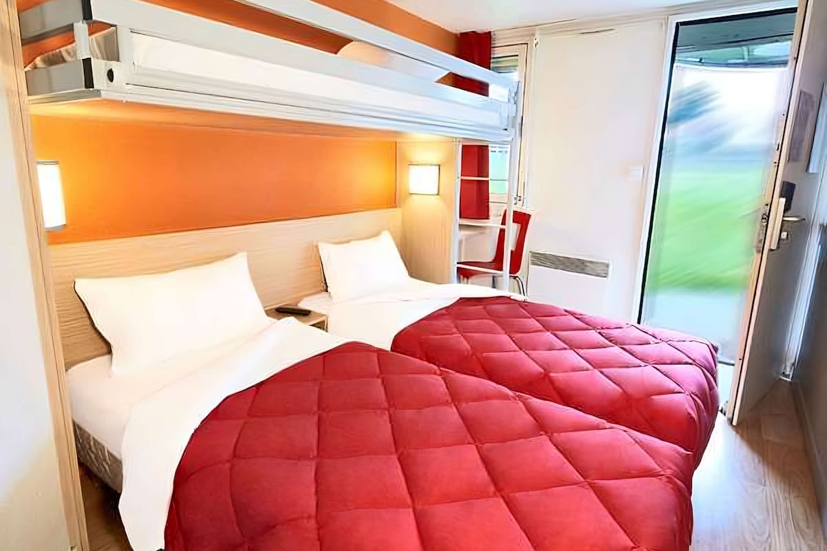 A hotel room with two beds, a red bedspread, a wooden headboard, a red chair, and a sliding glass door leading to a balcony.