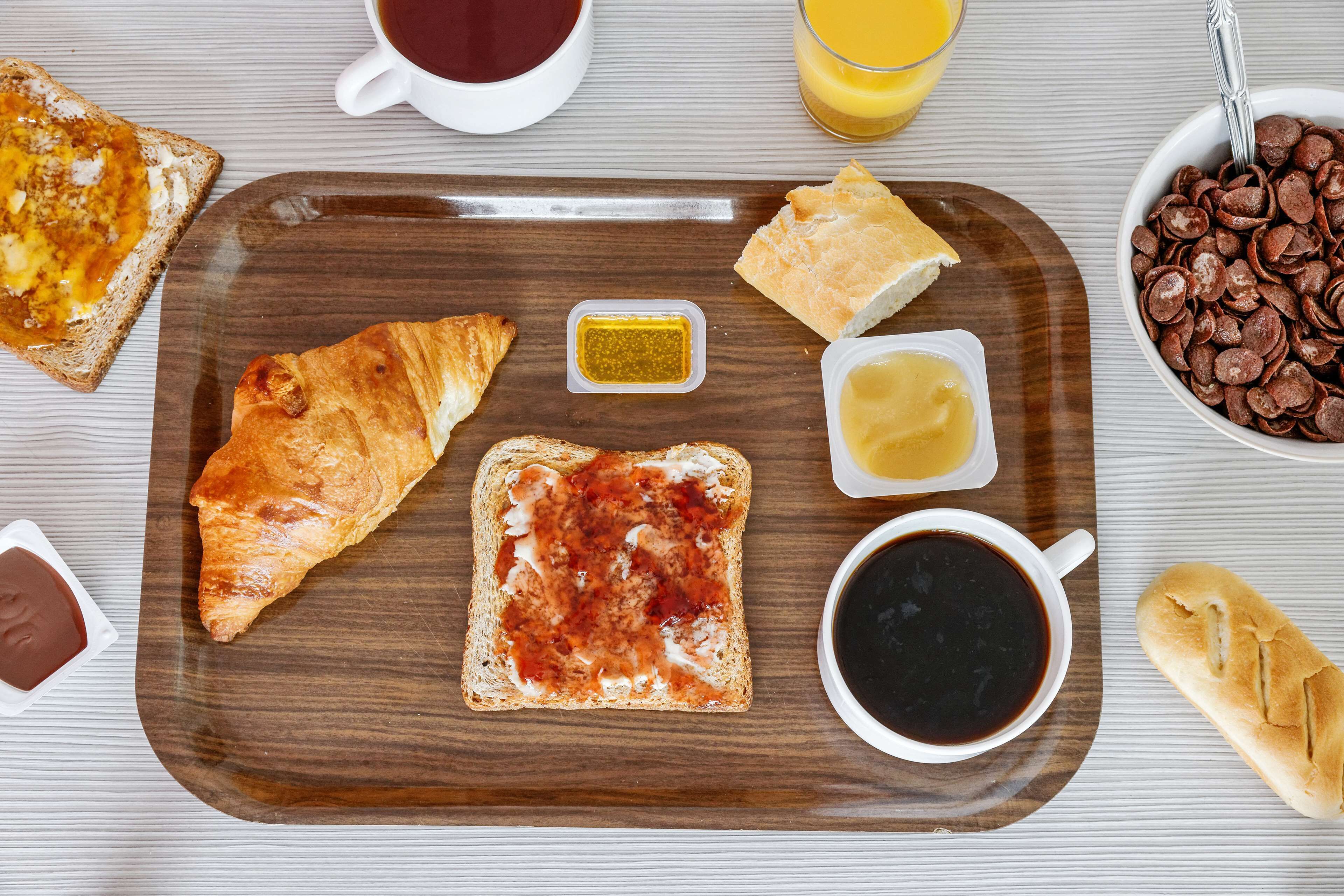 Een ontbijtplateau met croissants, boter, jam, koffie en een glas sinaasappelsap.