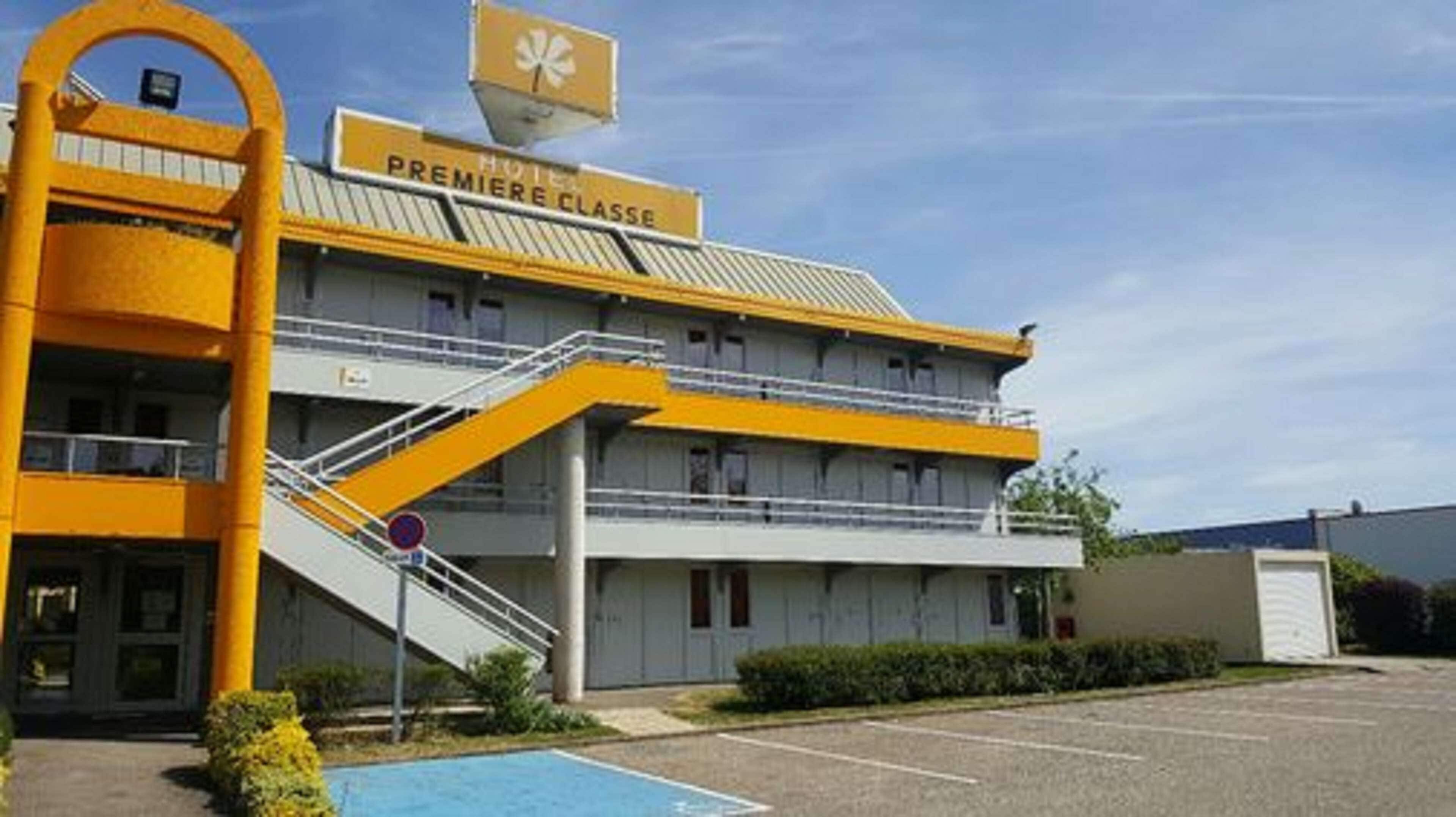 Un hotel con un ingresso giallo ben visibile, un cartello con la scritta "HOTEL PREMIERE CLASSE" e una scalinata che conduce all'ingresso.