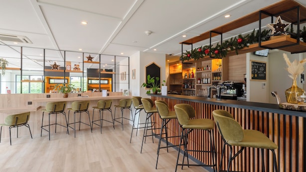 A modern bar area with wooden bar counters, green bar stools, and a decorative garland. - Premiere Classe Metz Sud - Jouy-Aux-Arches (Jouy-aux-Arches)