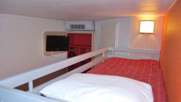 A single-bed room with a red bedspread, white bedding, a mounted television, and a wall-mounted air conditioner.