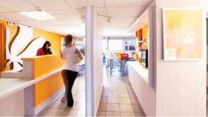 A modern interior with a reception desk, a counter with a menu, and a bright, open space. - Premiere Classe Metz Sud - Jouy-Aux-Arches (Jouy-aux-Arches)