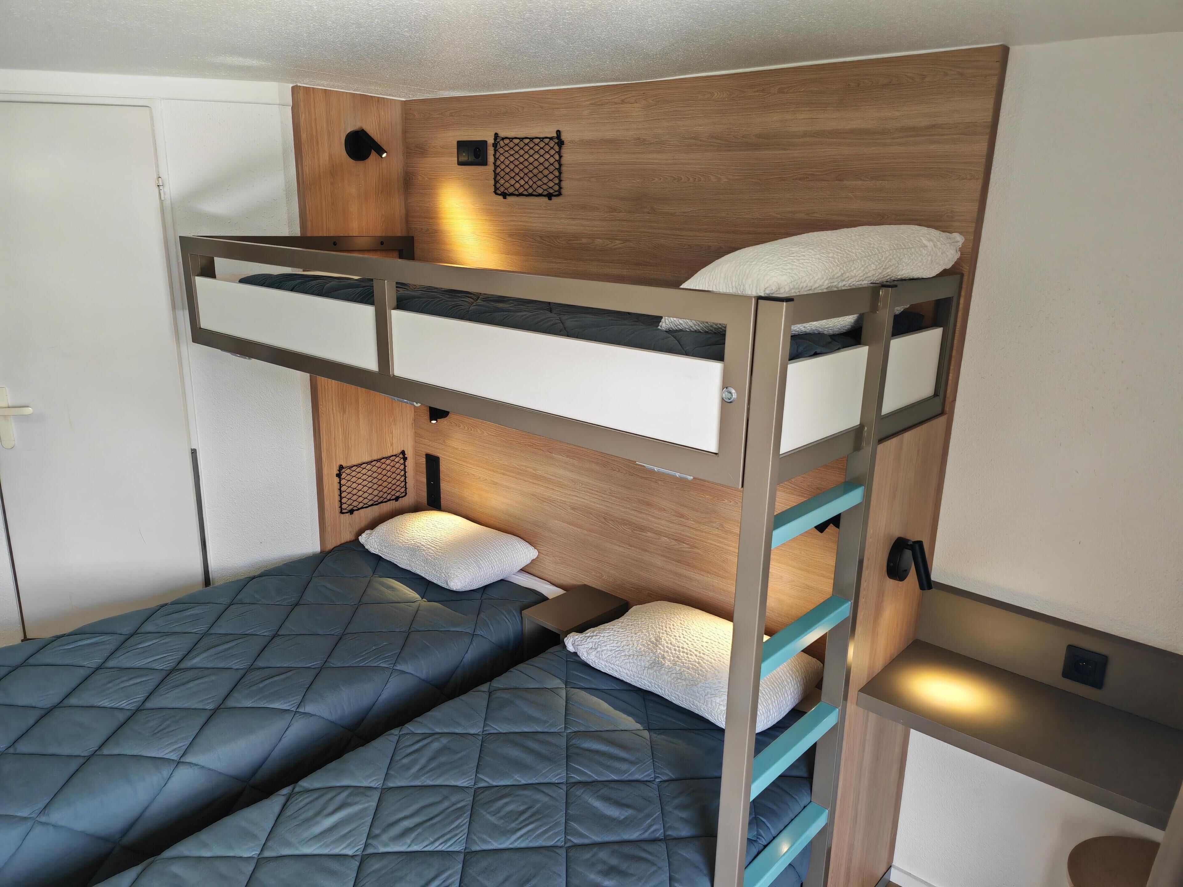 Una litera con cabecera de madera, un estante pequeño y una lámpara fijada a la pared.
