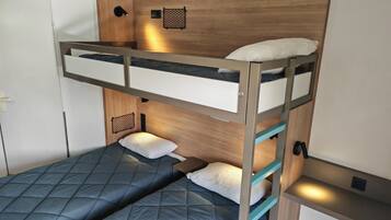Ein Stockbett mit Holz-Kopfteil, einem kleinen Regal und einer Wandleuchte.
