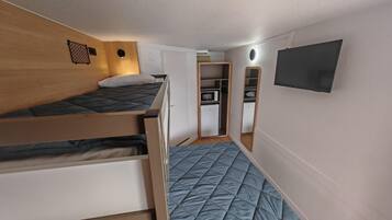 A compact room with a bunk bed, a small kitchenette, and a mirror on the wall.