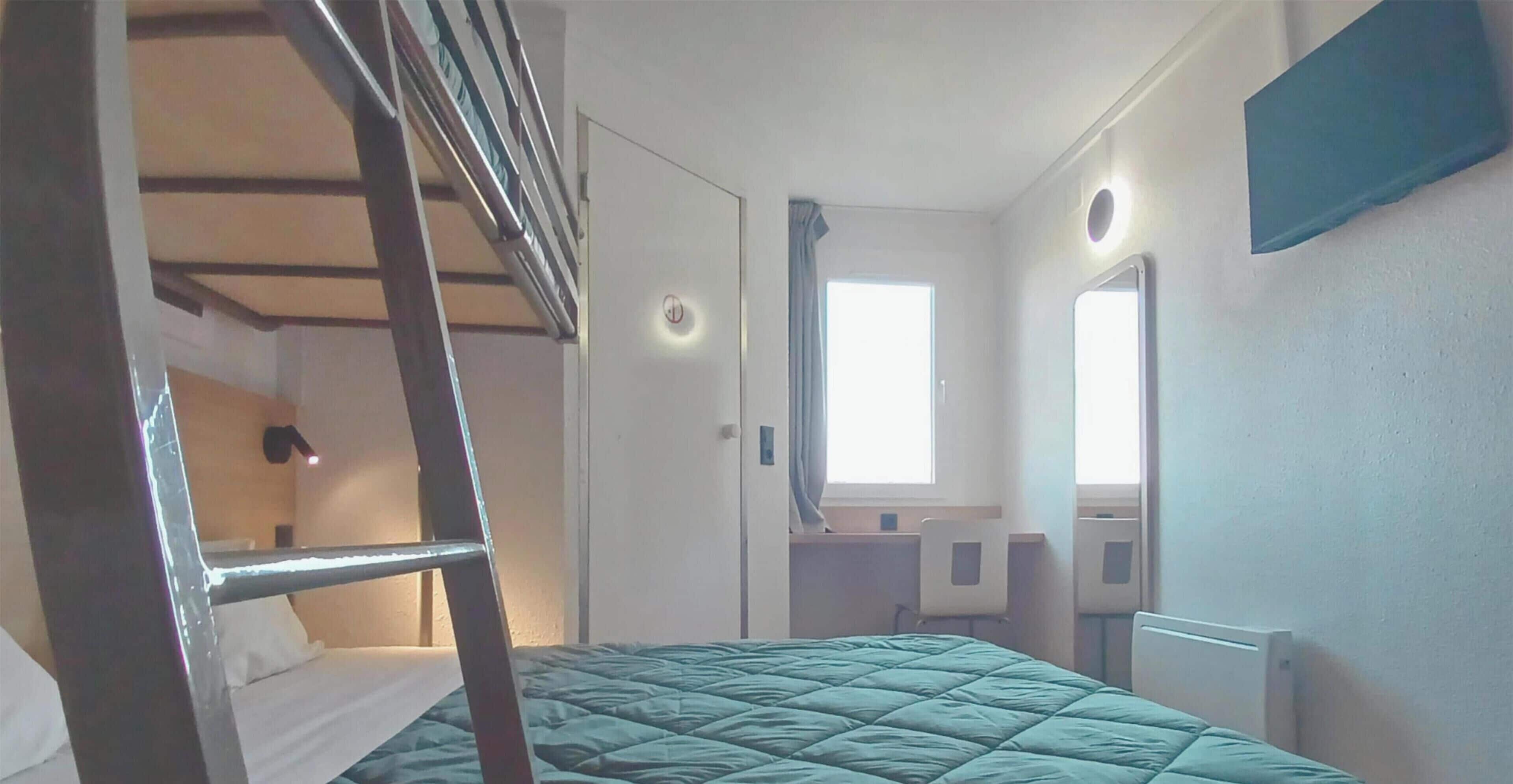 Een kamer met een stapelbed, een bureau, een stoel, een raam en een radiator.