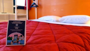 A hotel room with a red bedspread, a brochure on the bed, and a white headboard.