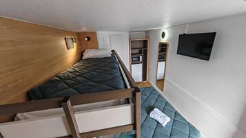 Een compacte slaapkamer met een stapelbed, een klein kitchenette, een spiegel en een televisie.