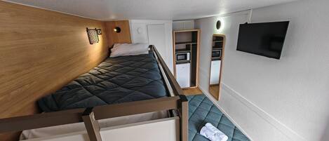Un dormitorio pequeño con literas, un kitchenette, un espejo y un televisor.