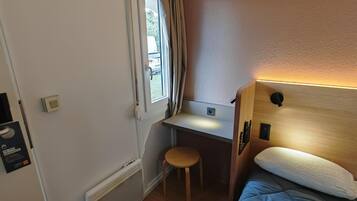 A compact room with a bed, a small desk, and a window.