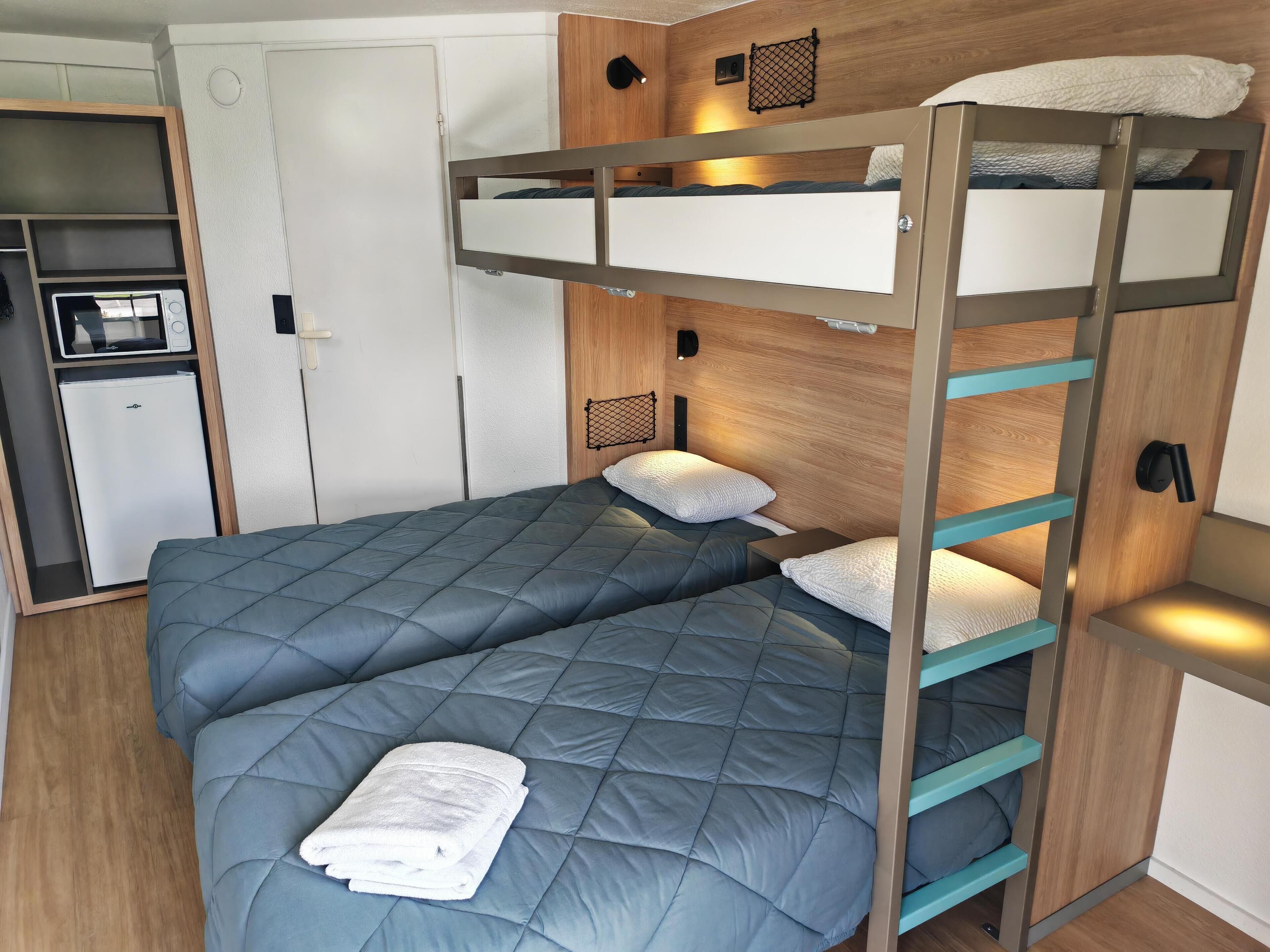 A bunk bed with a lower bed and a higher bunk, both with blue bedding. There is a white towel on the lower bed.