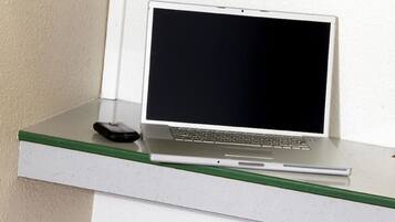 A laptop on a white shelf with a green edge, a black object next to it, and a white wall in the background.