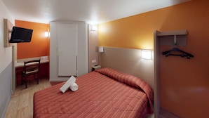 A hotel room with a bed, a desk, a chair, a TV mounted on the wall, and a wardrobe.