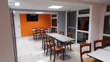 Un'area pranzo con diversi tavoli e sedie, una televisione montata a parete e una porta con un cartello.