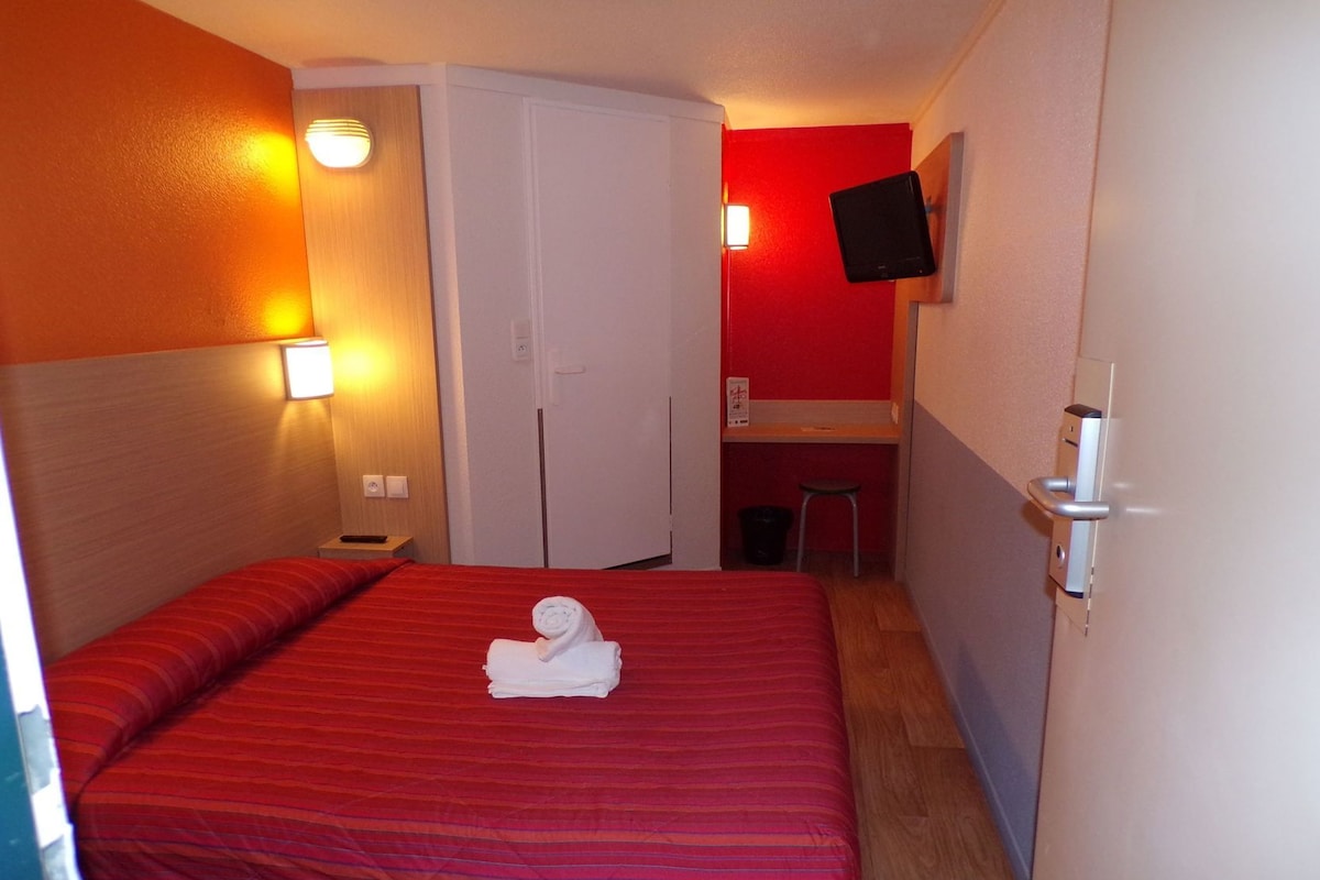 Een hotelkamer met een bed, een bureau, een televisie en een kledingkast.