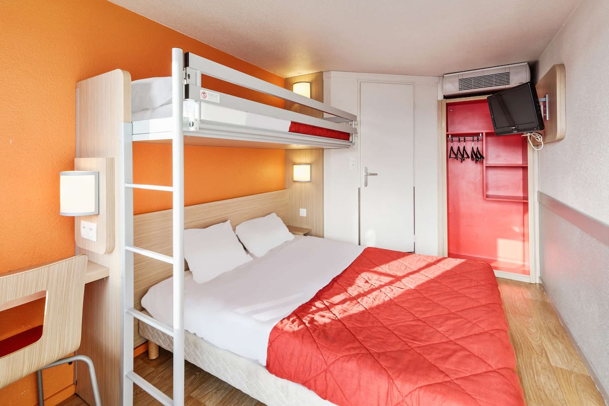 Habitación con literas, una manta roja, un escritorio, un armario y un televisor montado en la pared.