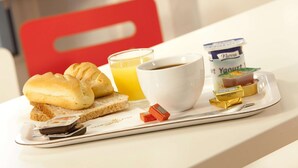 Ein Frühstückswagen mit Toast, Croissants, einem Glas Orangensaft, einer Tasse Kaffee, einem Becher Joghurt und einer kleinen Butterpackung.