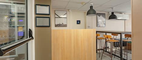 A modern office space with a wooden reception desk, framed cityscape artwork, and a bar area with stools.