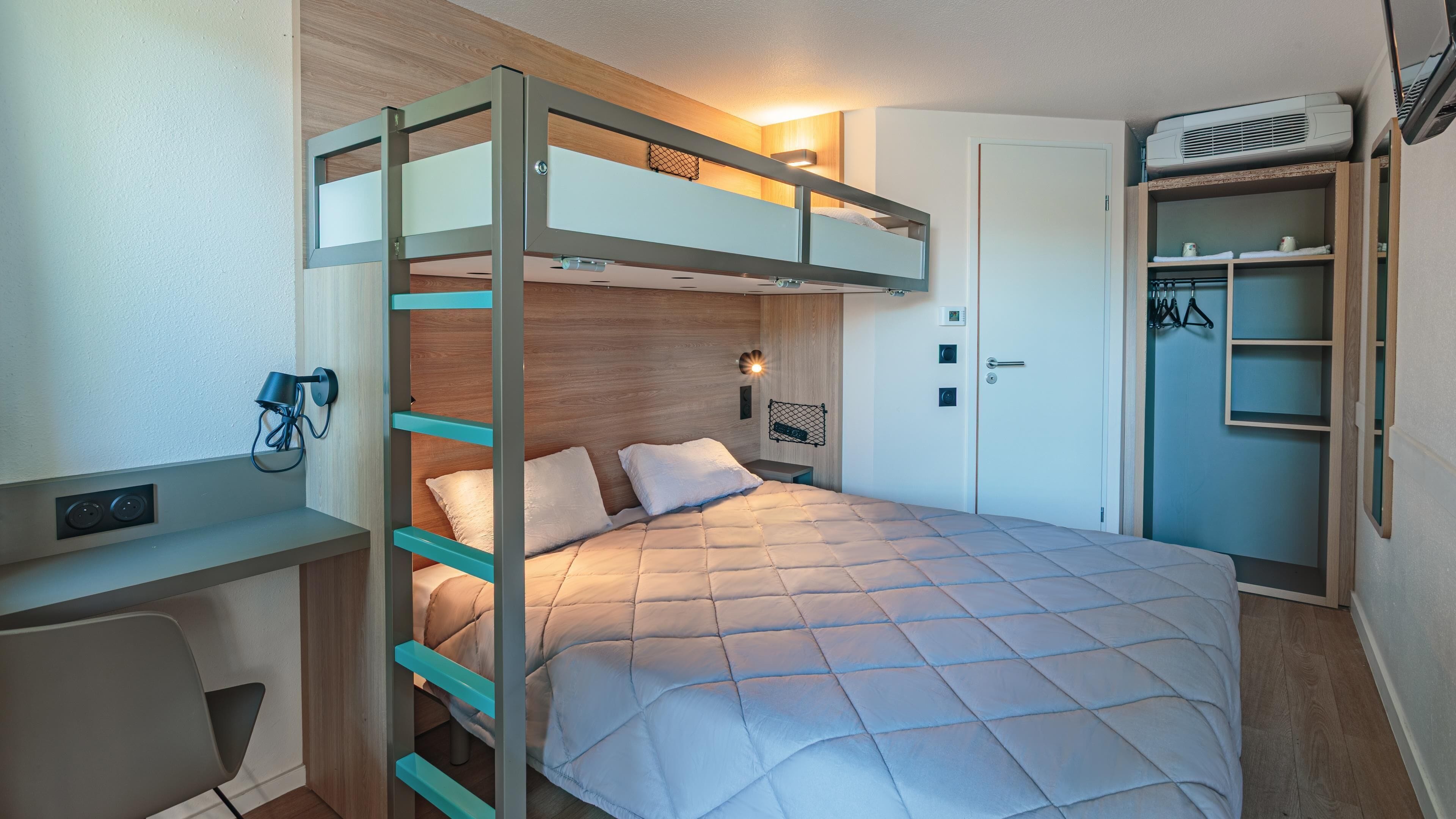 A bunk bed with a desk, a wardrobe, and a wall-mounted air conditioner.