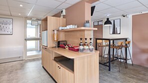 Cozinha moderna com bancada de madeira, geladeira e máquina de café. Há banquetas e uma pequena mesa de jantar com cadeiras.