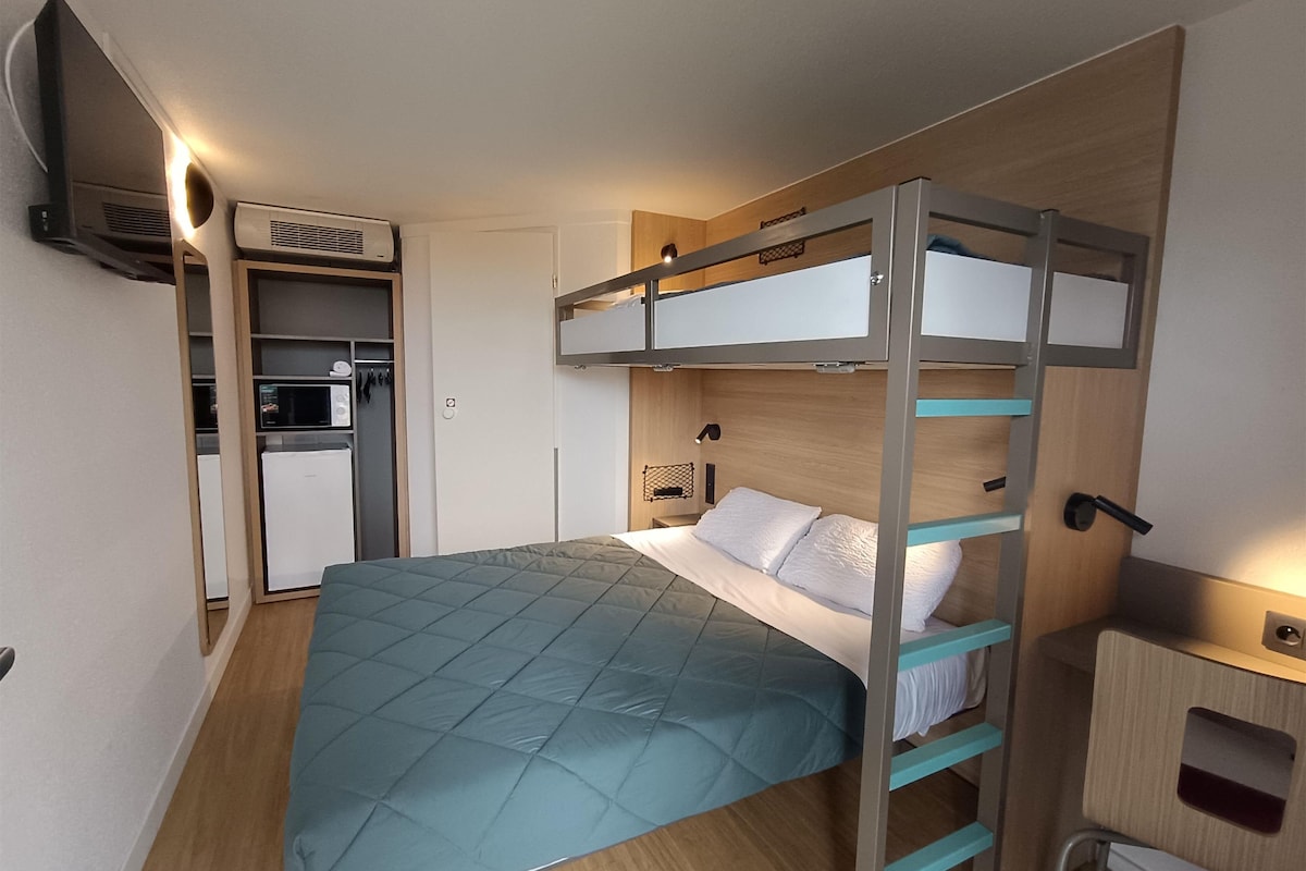Une chambre avec un lit superposé, une couette turquoise, un bureau avec une chaise et une armoire.