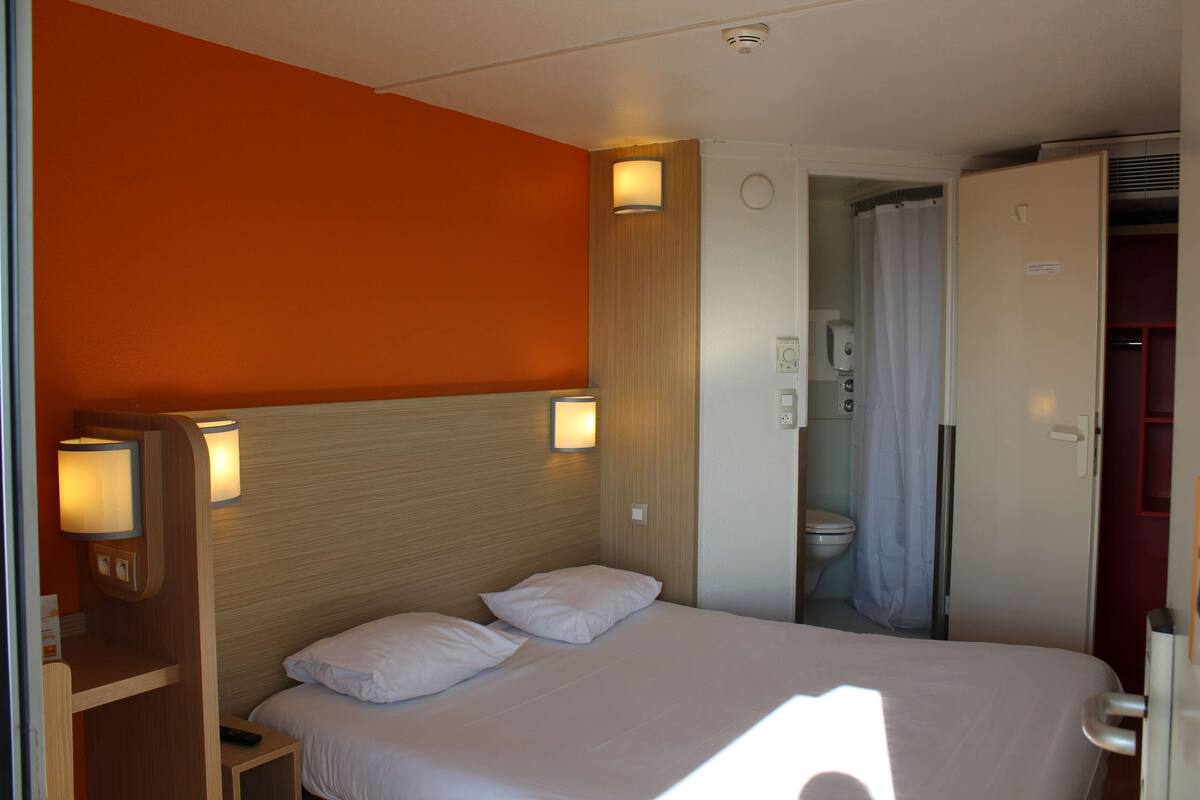 Une chambre d’hôtel avec un lit, deux lampes de chevet, une douche et des toilettes.