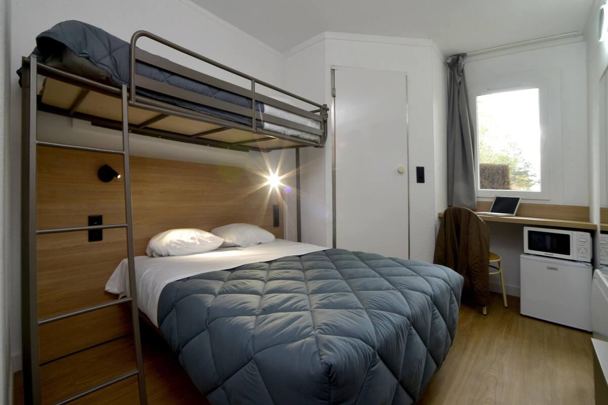 Une chambre avec un lit superposé, un bureau et un four à micro-ondes.