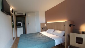 Une chambre d’hôtel moderne équipée d’un lit, d’un bureau, d’une armoire et d’une télévision.
