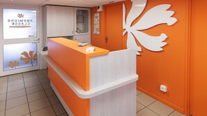 Un comptoir d’accueil aux couleurs blanc et orange, une grande feuille décorative sur le mur et un panneau indiquant la section « Première classe ».