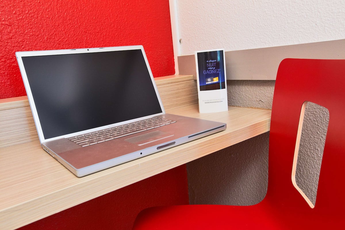 A laptop on a wooden desk with a red chair.