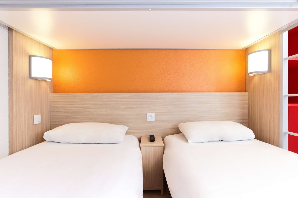 A hotel room with two beds, a wooden headboard, and a red accent wall.