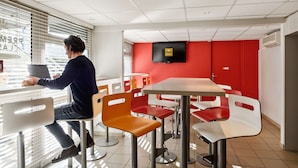 A modern dining area with a person using a tablet, surrounded by red and white chairs, and a flat-screen TV mounted on the wall.