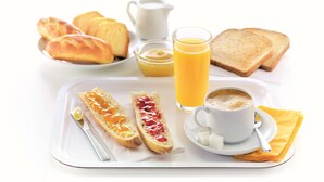 A breakfast tray with croissants, toast, jam, butter, a glass of orange juice, and a cup of coffee.