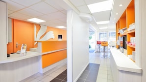 A modern reception area with a white counter, orange accents, and a view of the outdoors.