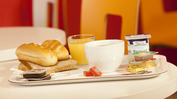 A breakfast tray with croissants, orange juice, a cup, yogurt, and butter on a white table.