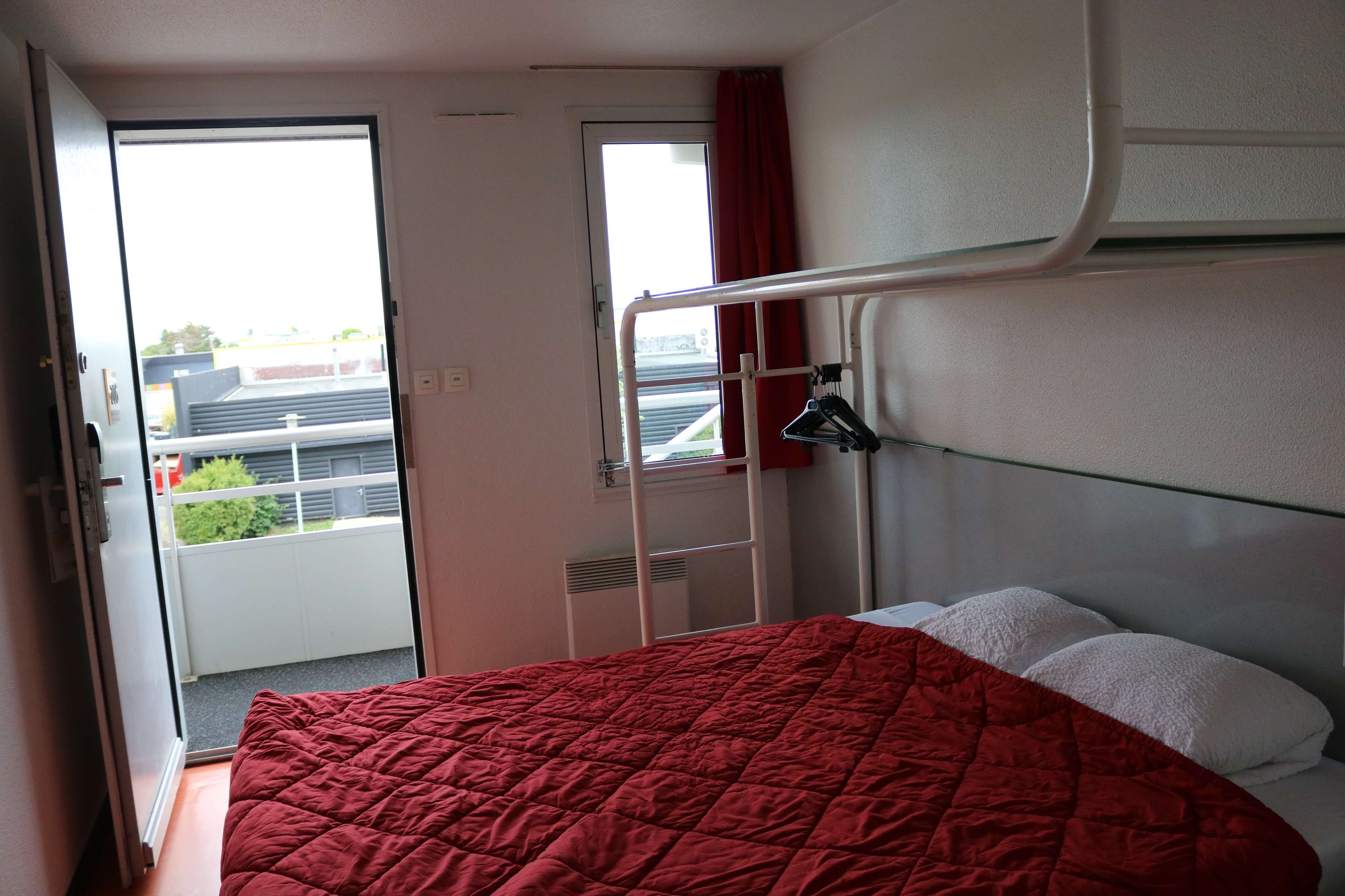 Quarto compacto com beliche, porta para uma varanda e janela com cortina.