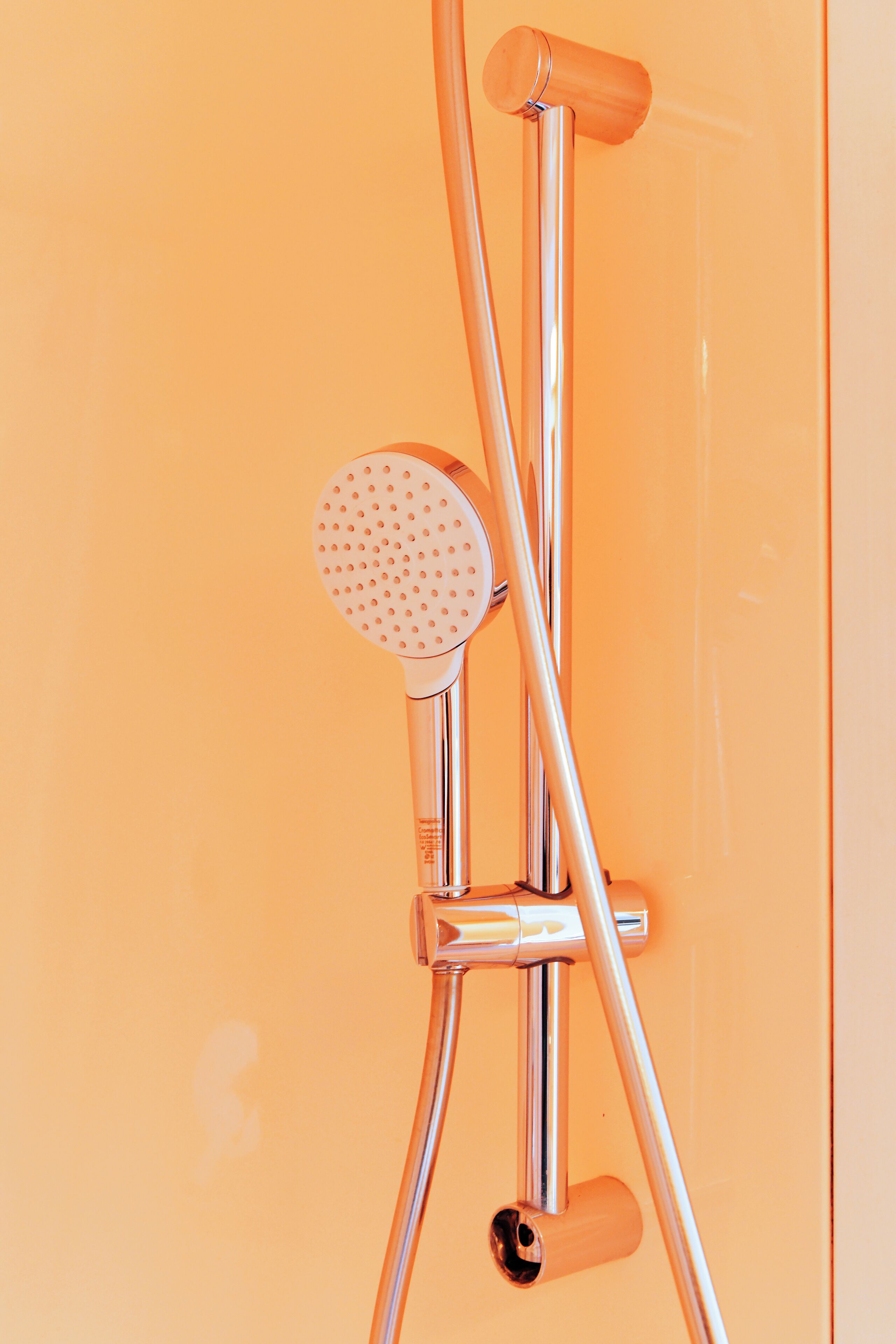Douchekop van chroom met een rond, geperforeerd ontwerp, bevestigd aan een muur met een glad, oranje oppervlak.