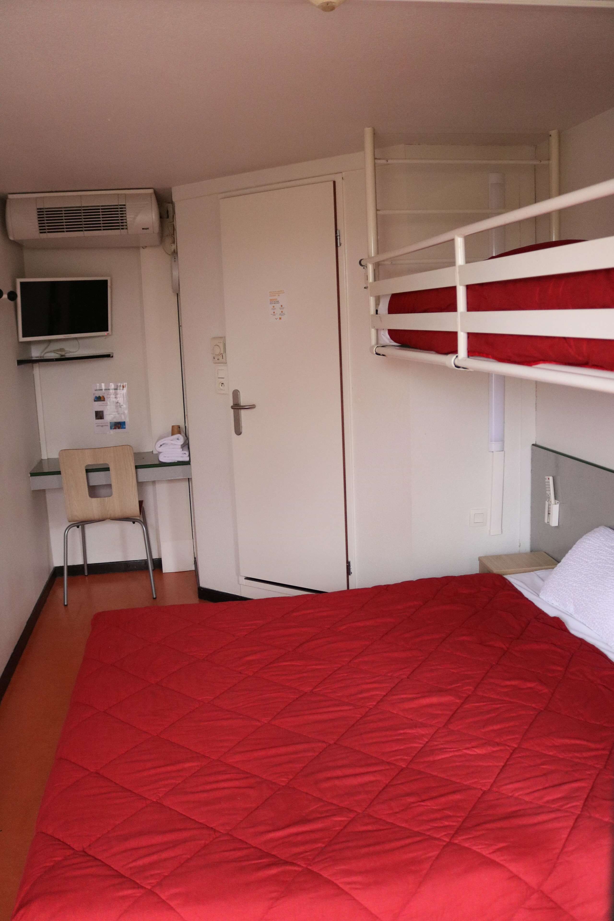 Una habitación con literas, un escritorio con silla, un televisor y una puerta.