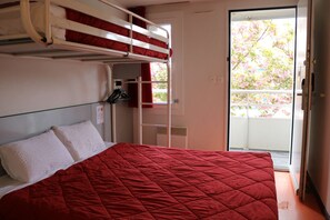 A bunk bed room with a red quilted bedspread, a white pillow, and a red curtain.