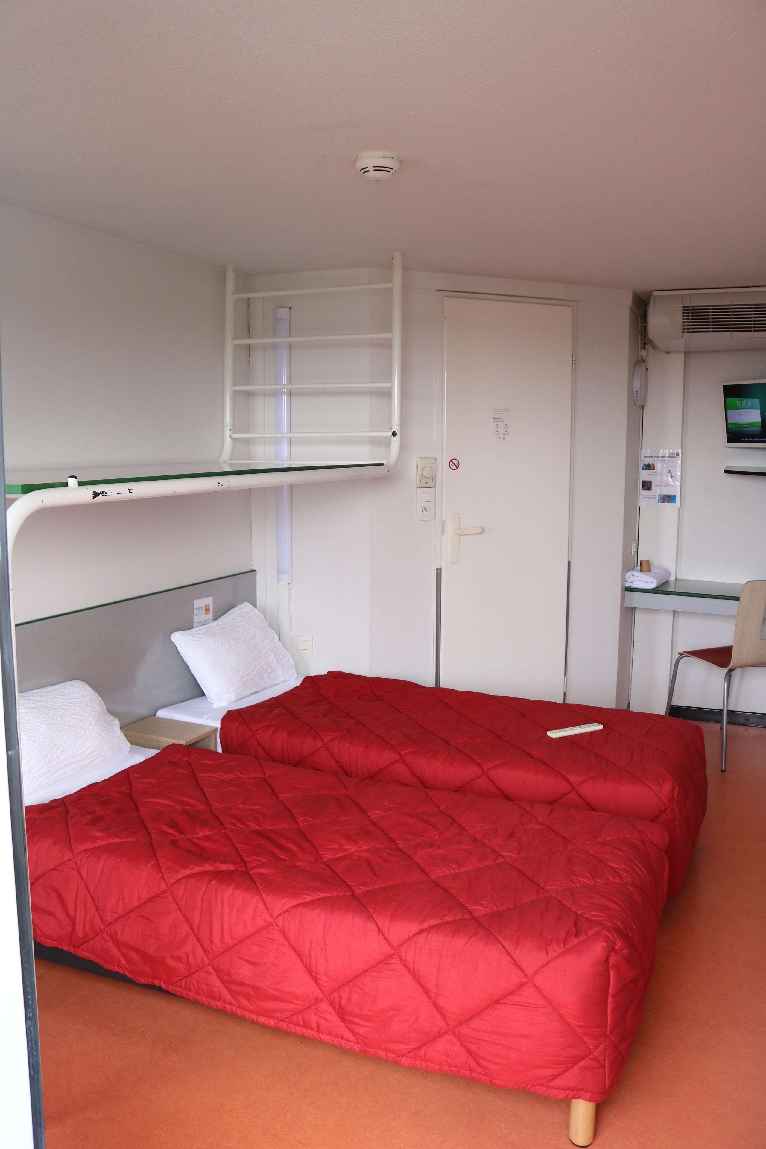 A hotel room with a bunk bed, a desk with a computer, and a chair.