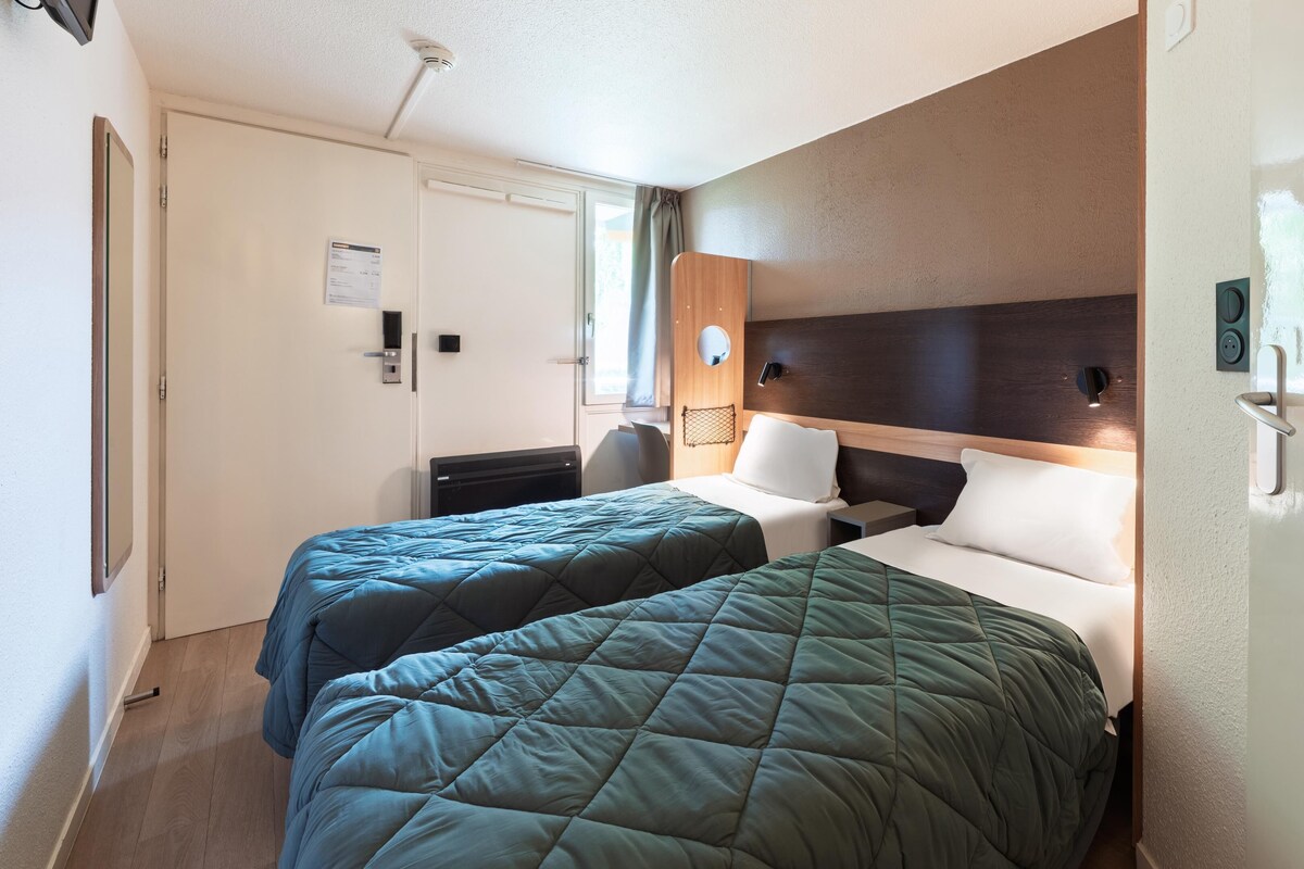 Une chambre d’hôtel avec deux lits, un bureau et une chaise.
