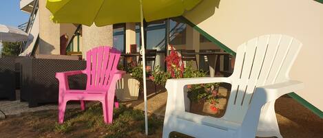 Outdoor seating with a yellow umbrella, two Adirondack chairs, and a planter with flowers.