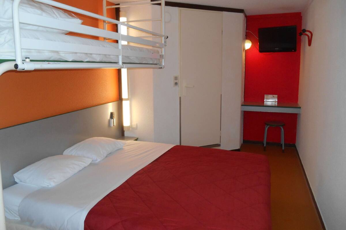 Una habitación de hotel con literas, un escritorio, un televisor y una pared de acento roja.