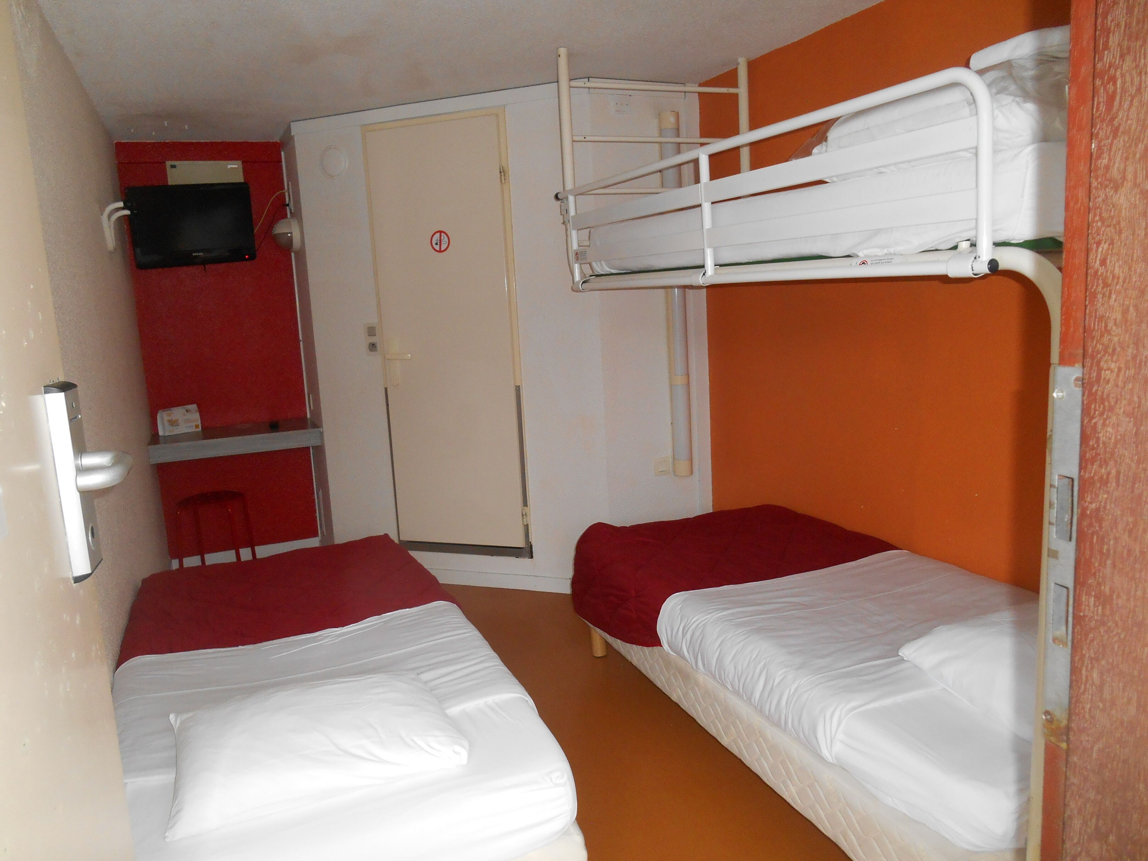 Un dormitorio con literas, televisión, una puerta y una pared roja.