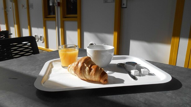 Bandeja de desayuno con un croissant, un vaso de jugo de naranja y un bol sobre una mesa, con una ventana al fondo.