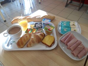 Bandeja de desayuno con croissants, jamón, jugo y yogur sobre una mesa de madera.