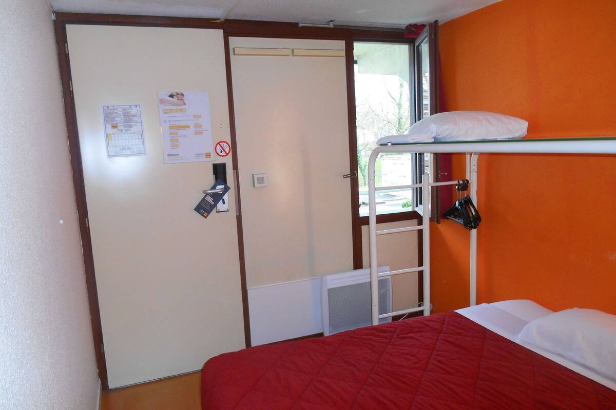 Una habitación pequeña con literas, una puerta con un aviso y una ventana con vistas.