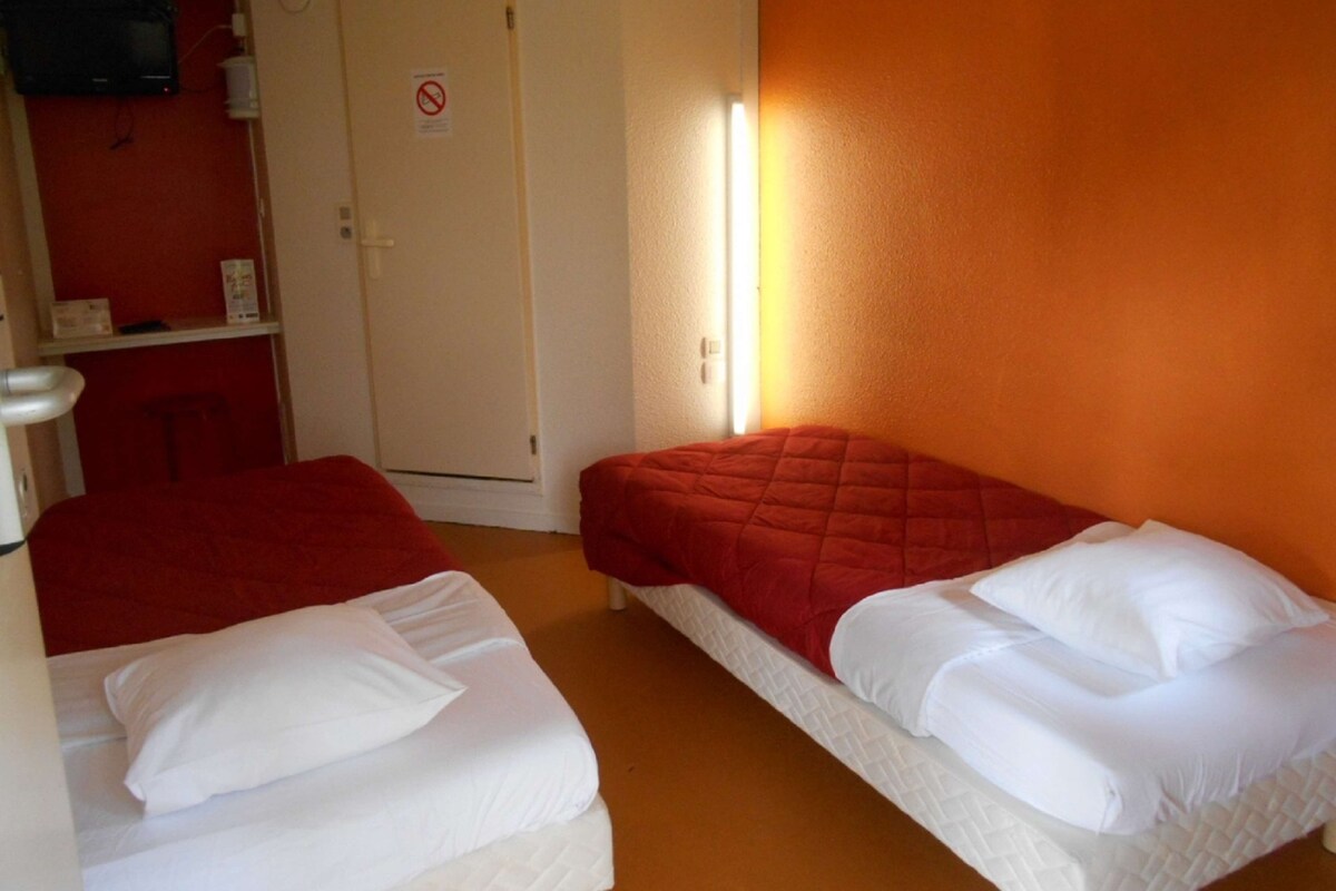 Ein Zimmer mit zwei Betten, einer roten Wand, einer weißen Tür und einem an der Wand montierten Projektor.