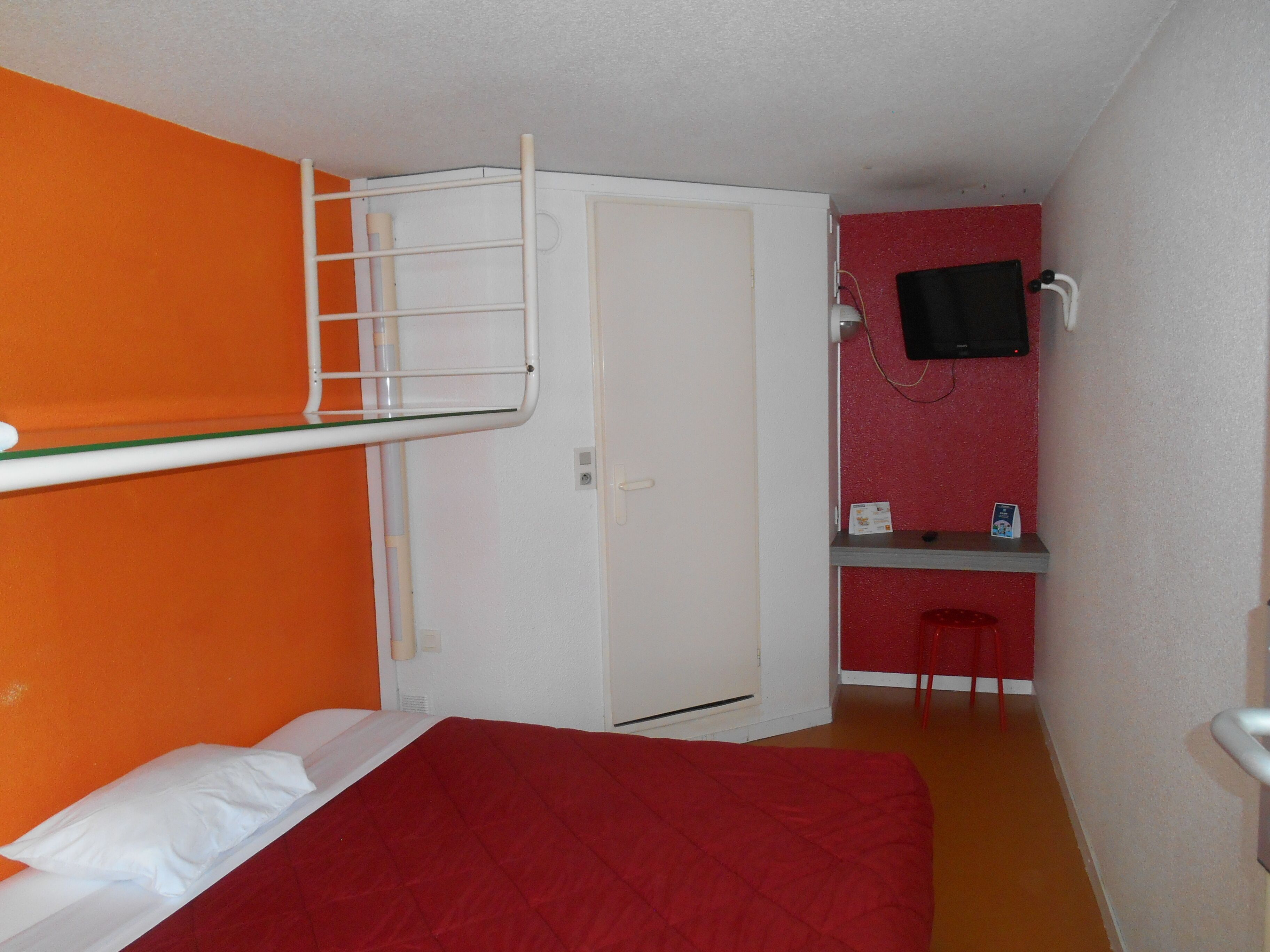 Una habitación pequeña con una cama litera, un escritorio con una silla y un televisor en la pared.